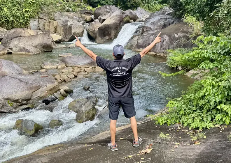 Guest with arms raised facing river cascades among boulders