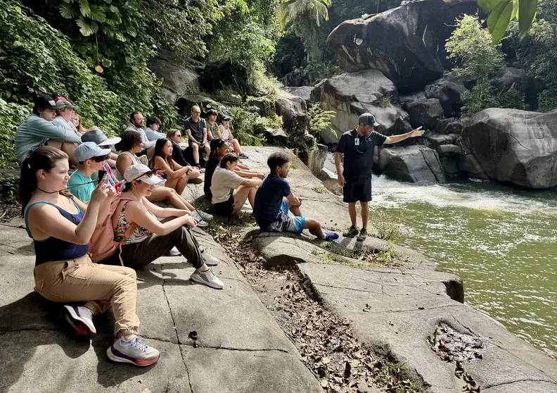 Guide speaking to a seated tour group beside the river on a guided El Yunque swimming tour