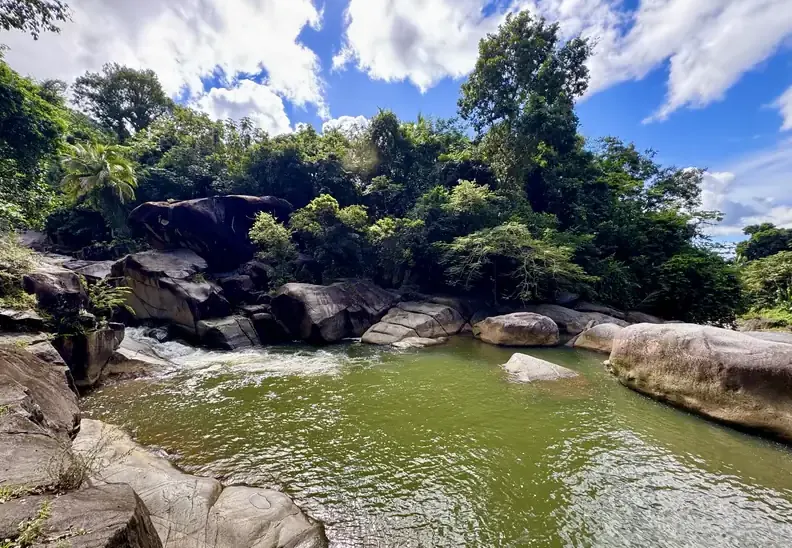 Wide, calm rainforest swimming hole framed by boulders and jungle on the swimming and waterfalls tour