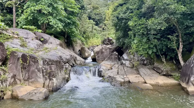 Small waterfall flowing between boulders into a swimming hole on the guided rainforest swimming tour