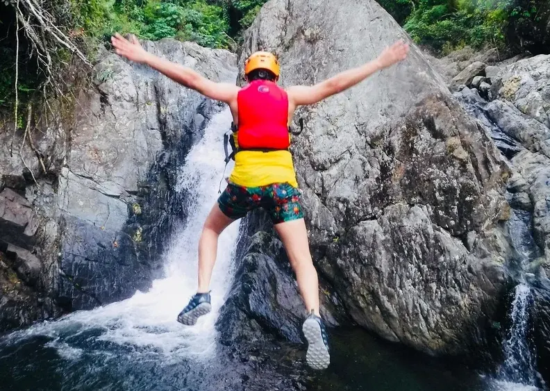 Guest leaping off a boulder beside a waterfall into the pool below