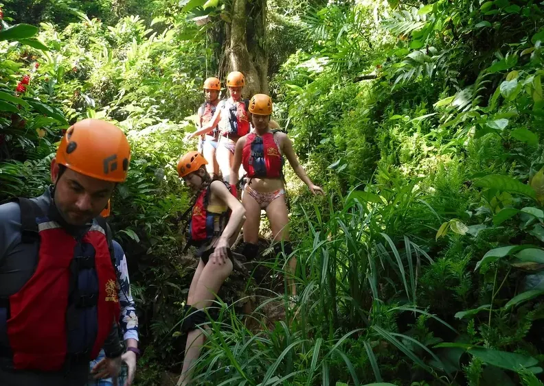 Guests in helmets and life jackets hiking through dense rainforest