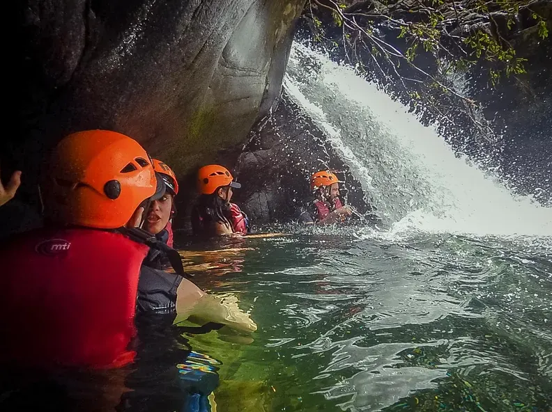 Guests in helmets swimming toward a waterfall in a rainforest pool