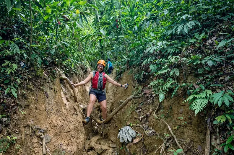Guest in a helmet walking a muddy rainforest trail in El Yunque